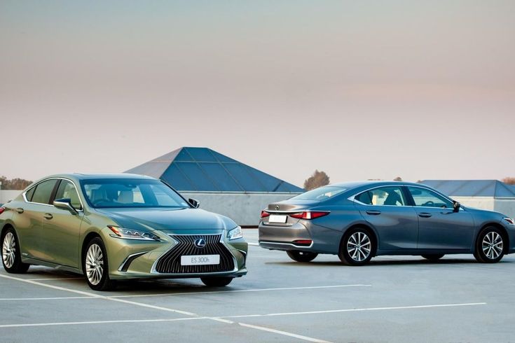 Two sleek, modern sedans parked on a rooftop with geometric skylights and a clear sky background. Luxurious automotive design showcased.