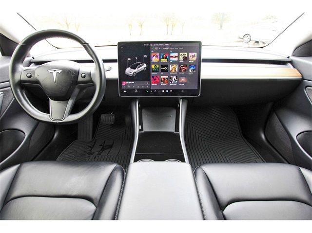 Tesla car interior showing sleek design with a touchscreen dashboard, black leather seats, and minimalist steering controls.