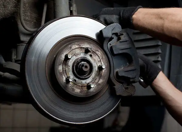 7 Ways Youre Ruining Your Car - Engine Stories Mechanic inspecting car brake disc and caliper in a garage. Automotive repair and maintenance.
