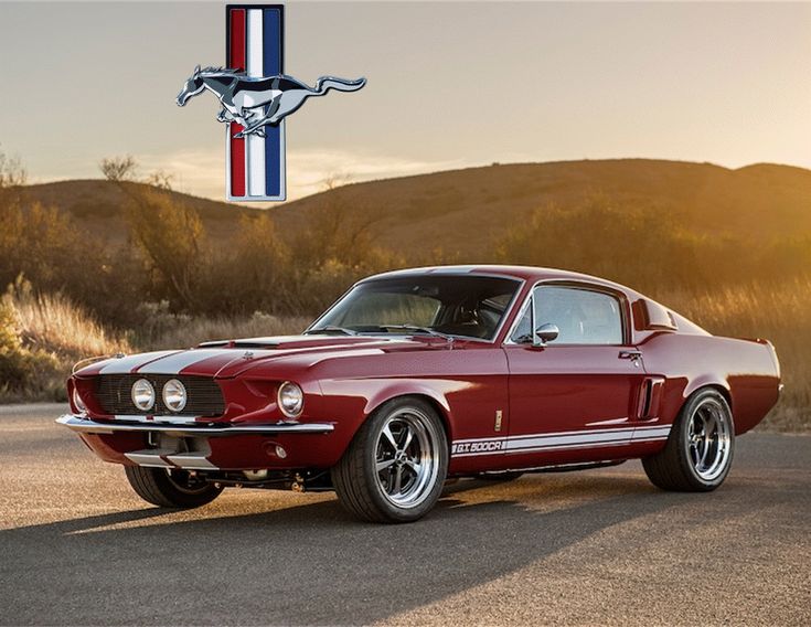 Vintage red Mustang GT500 car with racing stripes parked on a scenic road at sunset, iconic pony logo above.