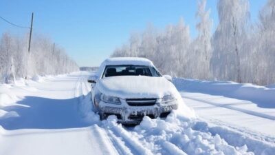 Car stuck in deep snow on a rural road surrounded by frosty trees, under a clear blue sky. Winter driving challenges.