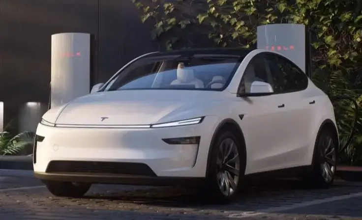 All-New 2025 Tesla Model Y Juniper Finally Revealed - Engine Stories White electric SUV parked at a Tesla charging station, showcasing sleek design and modern technology in a natural setting.