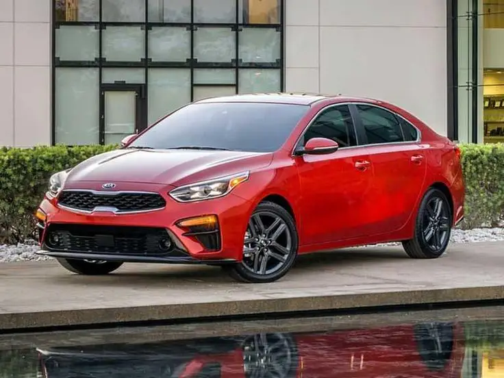 Calificación de seguridad del Kia Forte_ ¿Vale la pena_ - Engine Stories Red Kia sedan parked outdoors in front of modern building, highlighting sleek design and style.
