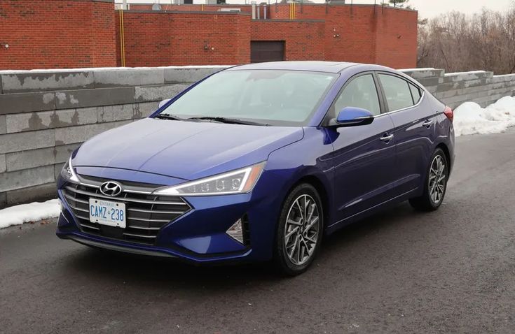 Blue Hyundai sedan parked on urban street with brick building background, showcasing sleek design and modern features.