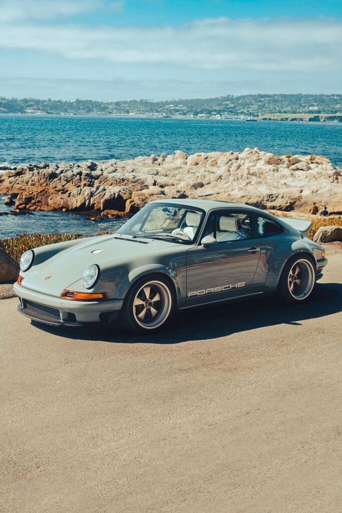 Vintage Porsche parked by a rocky coastal landscape with ocean view under a clear blue sky. Classic car, scenic drive.