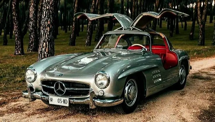 Do you like Vintage ⚡ - Engine Stories Classic silver sports car with gullwing doors open, parked on a forest path, showcasing vintage elegance and timeless design.