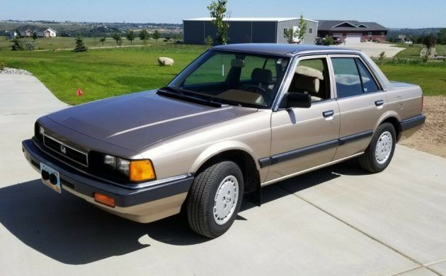 Classic beige sedan parked in a driveway, showcasing vintage automotive design with a scenic rural backdrop.