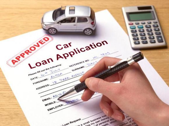 Car loan application approved with model car and calculator. Hand holding pen filling out details. Finance and loan approval concept.