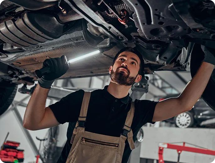 Mechanic inspecting car undercarriage with flashlight in auto repair shop. Vehicle maintenance and repair expert at work.