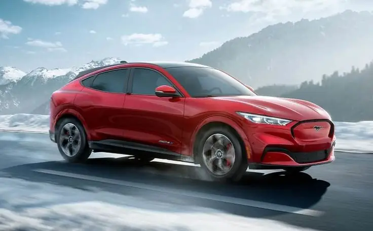 Mustang Mach-E ein Elektro SUV mit bis zu 465 PS - Engine Stories Red electric SUV driving on a snowy mountain road, showcasing sleek design and performance in wintry conditions.