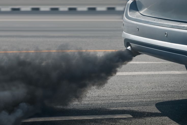 Car emitting thick black exhaust on road, illustrating vehicle pollution and environmental impact.