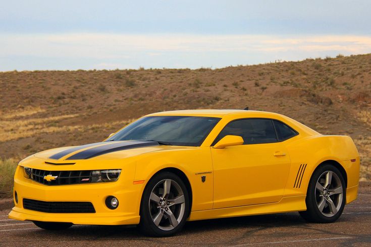 Yellow sports car with black racing stripes parked in a desert landscape under a cloudy sky.