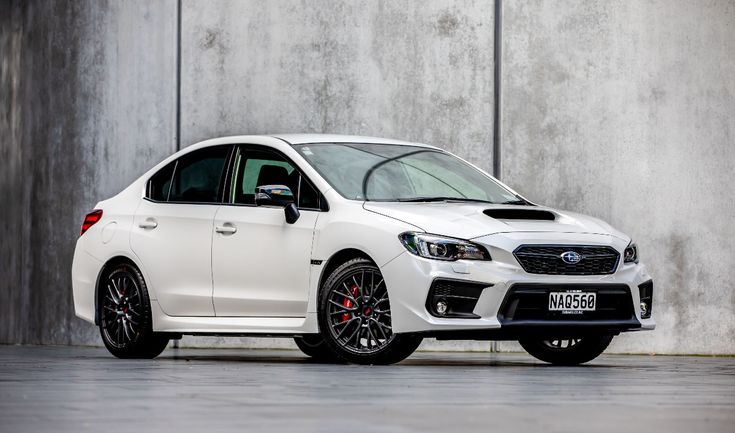 Sleek white sports sedan with aggressive styling, parked against a concrete wall, showcasing its modern design and alloy wheels.