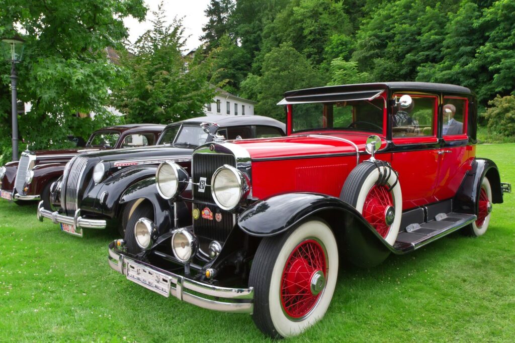 Vintage classic cars on lush green grass, showcasing elegant red and black designs against a backdrop of trees.