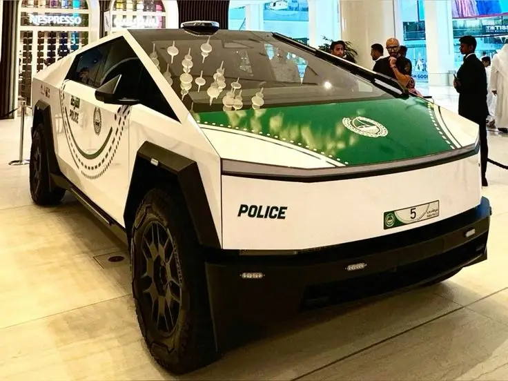 The Tesla Cybertruck - Engine Stories Futuristic police vehicle displayed indoors, featuring a sleek design and green accents, surrounded by onlookers.