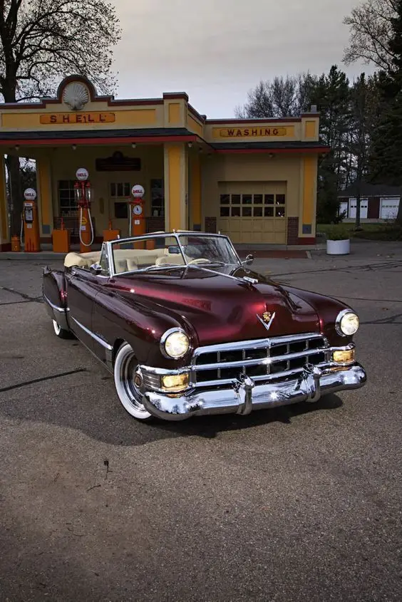 This 1949 Cadillac Convertible Is Classic on the Outside and Contemporary on the Inside - Engine Stories Classic maroon convertible parked in front of vintage Shell gas station, showcasing retro automotive elegance.