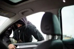 Hooded person attempting to break into a car, emphasizing vehicle security risks and prevention measures.