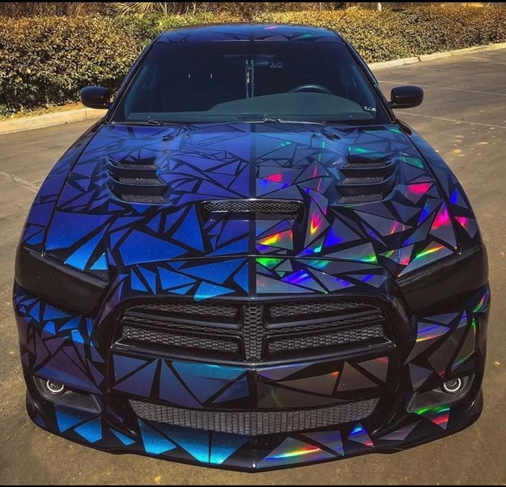 Sleek black car with vibrant, geometric holographic wrap parked outdoors. Eye-catching, futuristic design.