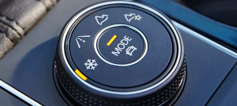 Close-up of a car drive mode selector knob showing options for different terrains and weather conditions.