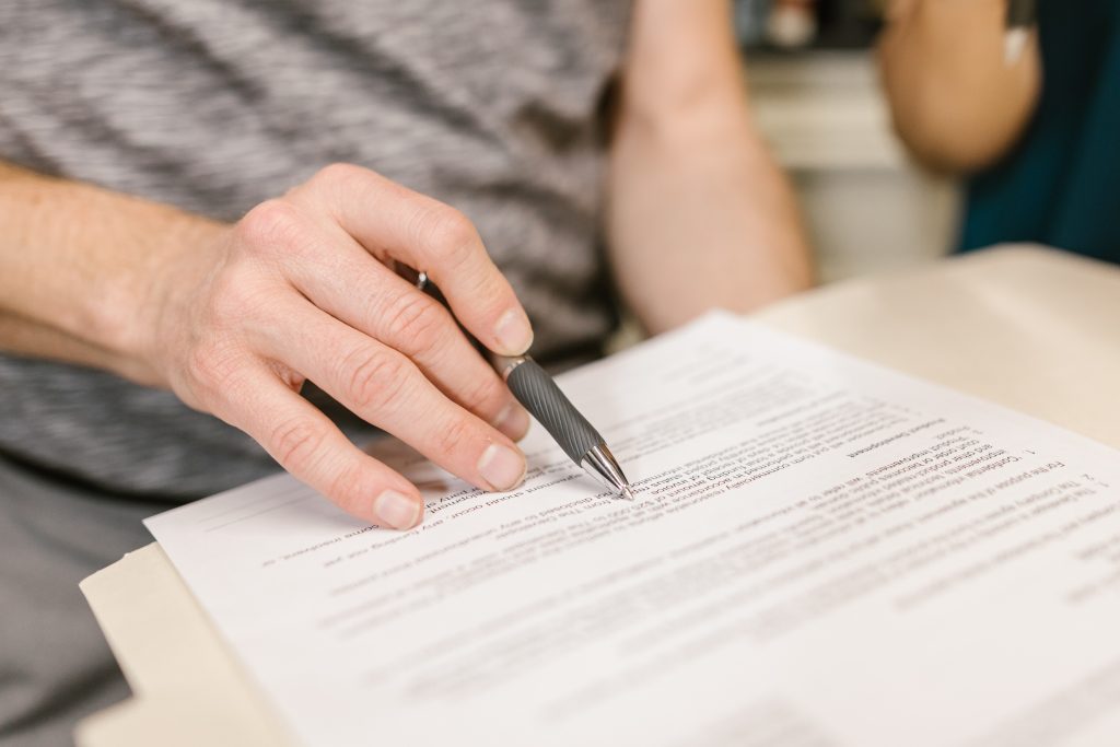 Hand holding a pen and pointing at document text, symbolizing agreement or review in a formal setting.