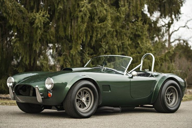 Classic green convertible sports car parked on a road, surrounded by lush greenery and trees in the background.