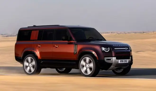 14df7ba4a70bf170dad9998c633cf3f2 - Engine Stories Red and black Land Rover Defender driving on a desert road, showcasing its off-road capabilities and rugged design.