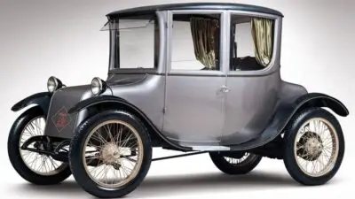 Vintage grey electric car with a classic design and spoked wheels, highlighting early 20th century automotive innovation.