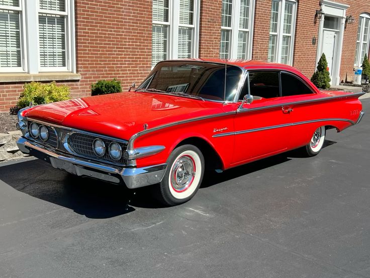1960 Edsel Ranger - Engine Stories Vintage red classic car parked in front of a brick building, showcasing sleek design and polished exterior.