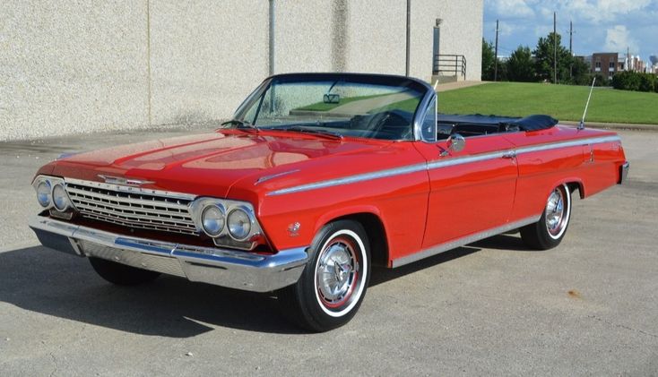 1962 Chevrolet Impala SS 409 - Engine Stories Red classic convertible car parked outdoors on a sunny day, showcasing its sleek design and chrome details.
