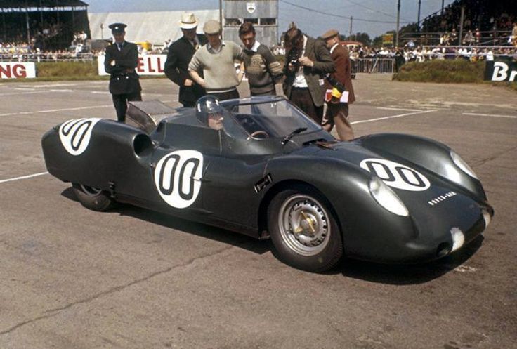 1963 LeMans Rover-BRM Turbine - Engine Stories Vintage sports car with racing number 00 at a classic car event, surrounded by onlookers and officials on a sunny day.