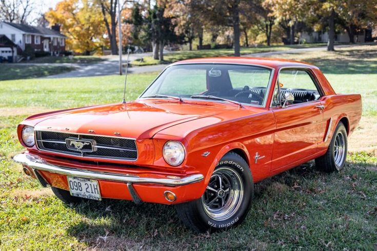 1964-1_2 Ford Mustang Coupe orange - Engine Stories Red classic 1966 Ford Mustang parked on grass with trees in the background on a sunny day.