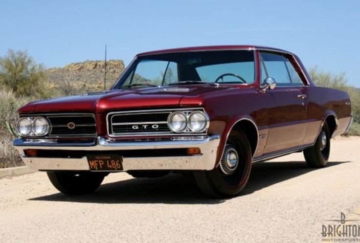 Classic red GTO car on a sunny desert road, showcasing vintage style and design.