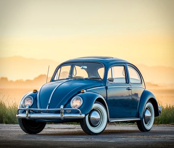 Vintage blue VW Beetle parked on a scenic road at sunrise, highlighting its classic design and iconic shape.