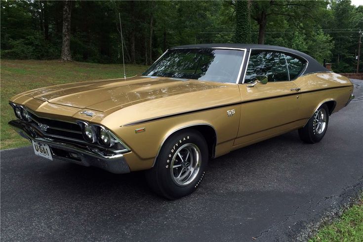 1969 Chevrolet Chevelle SS 396 © Barrett-Jackson - Engine Stories Vintage gold 1969 Chevrolet Chevelle SS parked on a road with lush greenery in the background. Classic American muscle car.