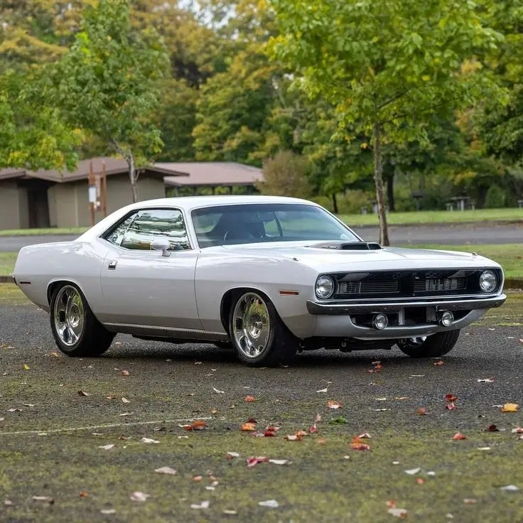 1970 Plymouth Barracuda 🔥 - Engine Stories Classic white muscle car parked in a scenic park with autumn leaves and green trees in the background.