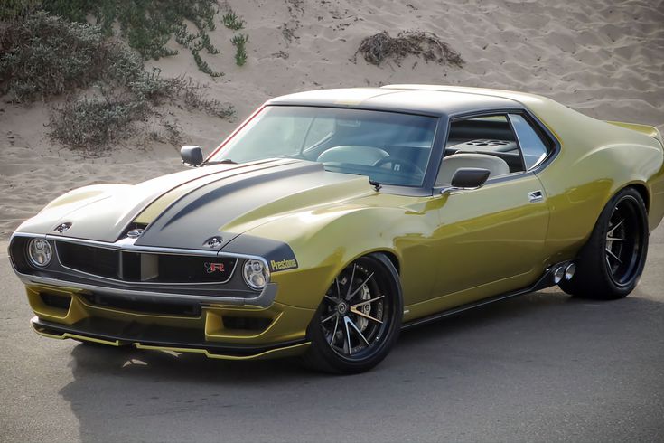 Vintage muscle car, olive green with black racing stripes, sleek design parked on street with sand dunes in background.