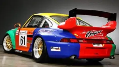 Vintage race car with colorful decals and large spoiler, showcasing number 61, ready for a motorsport event.