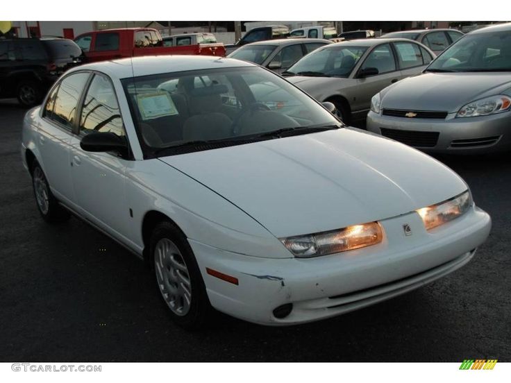 White sedan parked in a car lot, showcasing its front headlights and smooth body design.