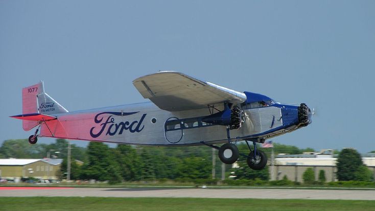 Vintage Ford Trimotor airplane taking off on a clear day, showcasing classic aviation design and engineering.