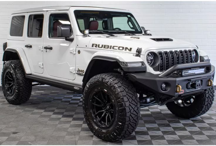 White Jeep Wrangler Rubicon with off-road tires, rugged design, parked indoors on tiled floor.