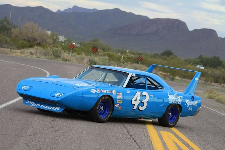 Vintage blue racing car with number 43 on winding desert road, featuring iconic design and bold sponsorship logos.