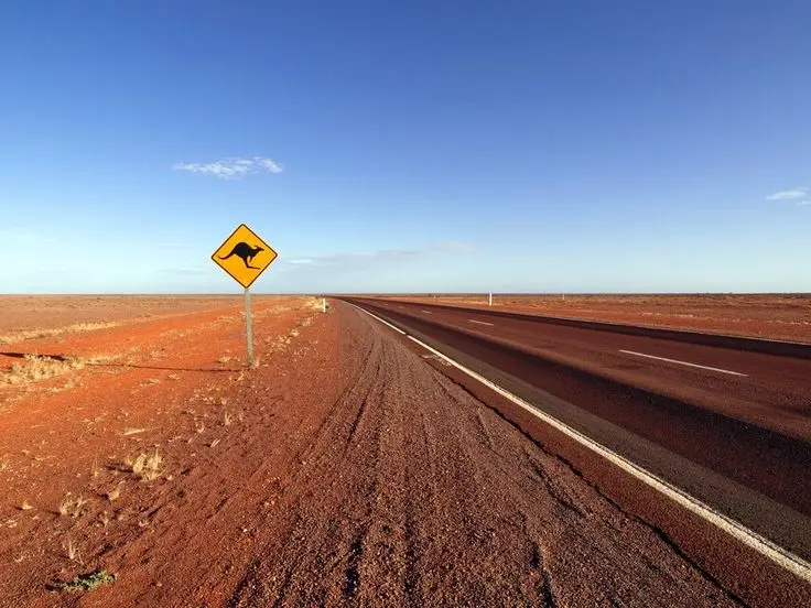 2e41b3666ed6c1d1a8e9b4f95a67ed14 - Engine Stories Open road in Australian Outback with kangaroo crossing sign under clear blue sky.