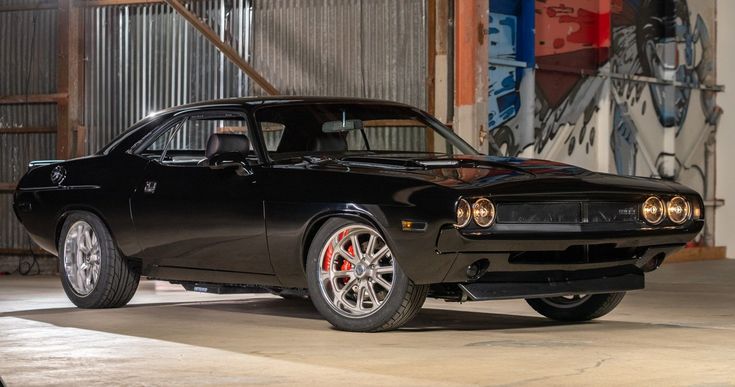 Classic black muscle car in a garage with murals, showcasing vintage design and sleek styling.