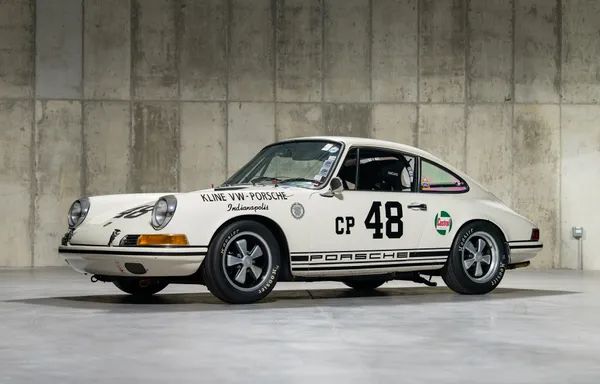 Vintage Porsche race car with number 48, white with black stripes, in front of a concrete wall. Classic design and sporty appeal.