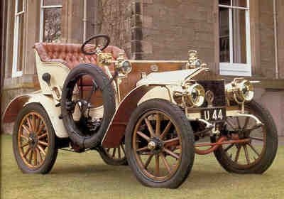 Vintage open-top car with wooden wheels and leather seats parked on grass, showcasing early 20th-century automotive design.