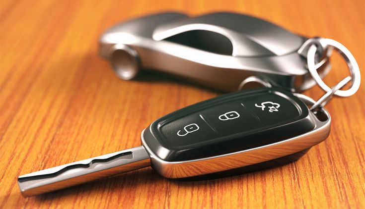 Close-up of a modern car key fob on a wooden surface with a small car keychain in the background.