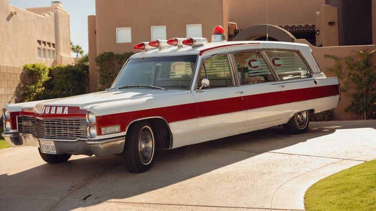 Vintage white and red ambulance parked on a sunny driveway, showcasing classic automotive design and nostalgia in a suburban setting.