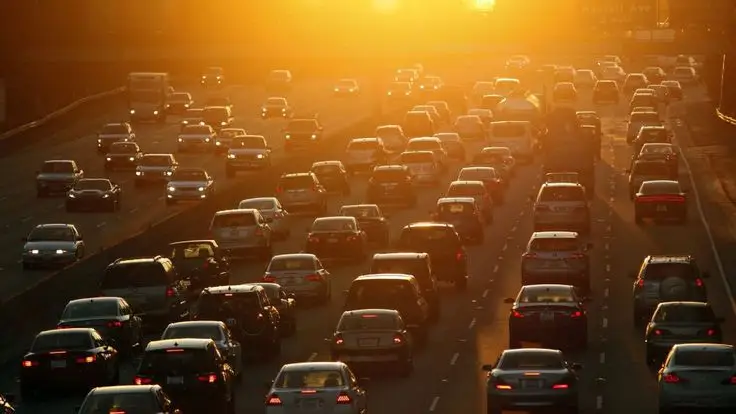 Heavy traffic on a highway at sunset, capturing the urban commute experience with cars lined up under a glowing orange sky.