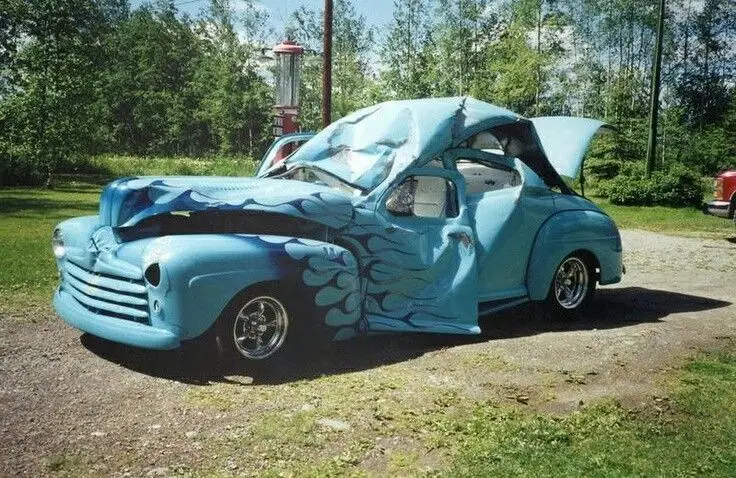 Unique blue custom car with open doors and hood, styled like waves, parked outdoors on a sunny day.