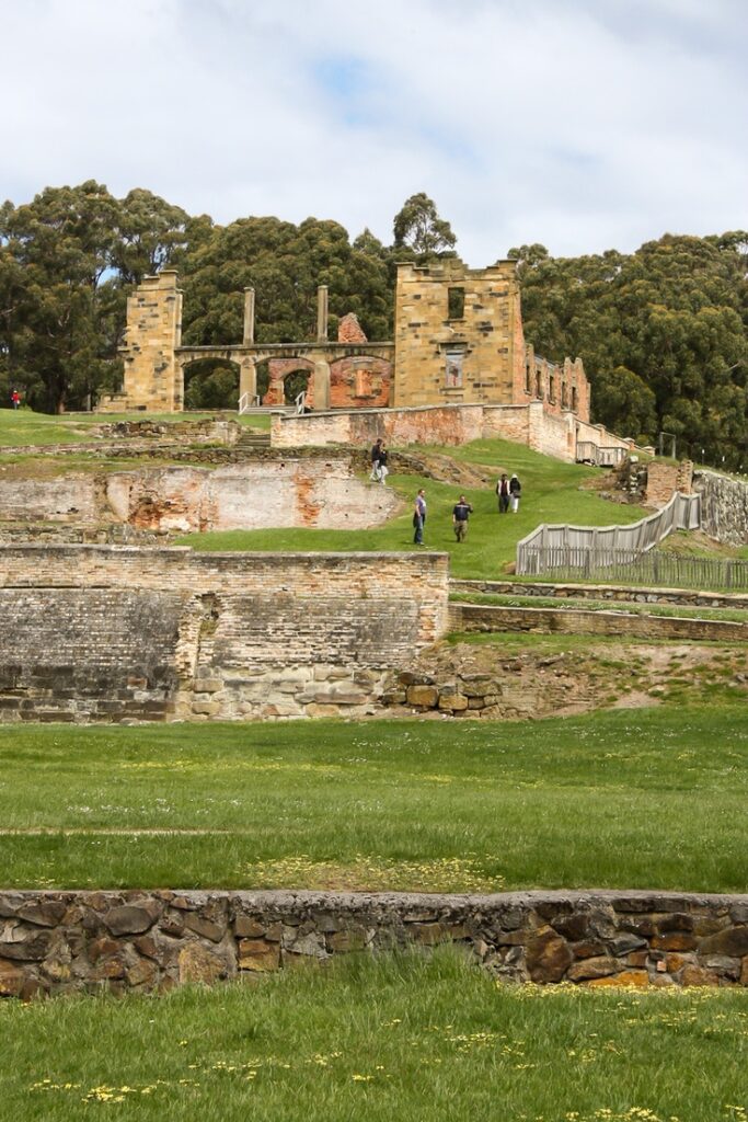 Historic ruins surrounded by greenery and trees, visitors exploring the site under a clear sky.